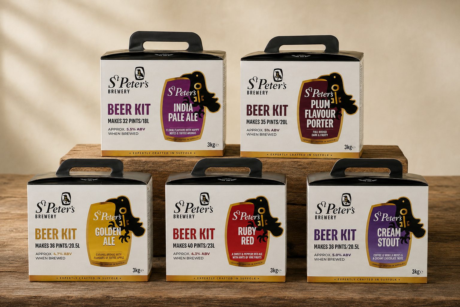 The five St Peter's Brewery kit boxes on a wooden bench — Golden Ale, Ruby Red and Cream Stout in front, India Pale Ale and Plum Flavour Porter on a plank behind — matching white carry-handle boxes, each with the raven-and-key emblem on its coloured barrel label.